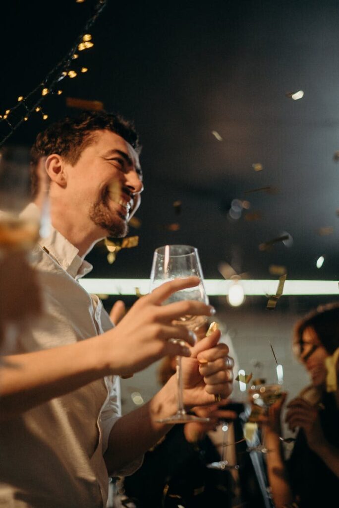 Joyful people celebrating New Year's Eve with drinks and confetti indoors.