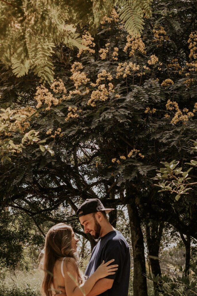 A loving couple embraces under a lush, flowering tree on a sunny day, capturing the essence of romance.