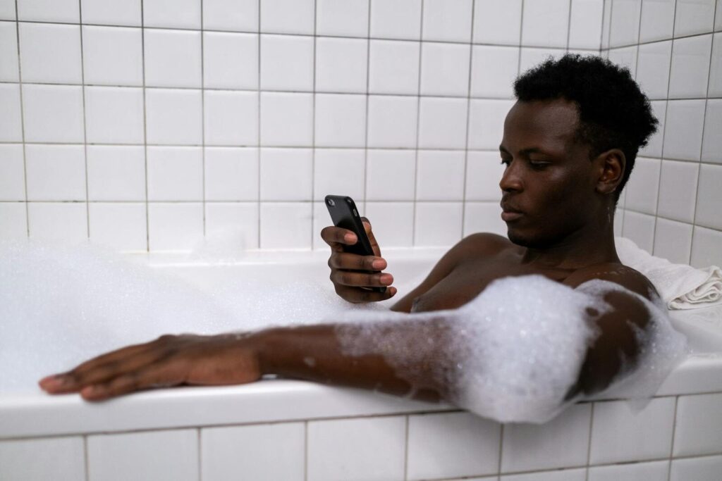 An adult man enjoys a relaxing bath while using a mobile phone, focusing on personal time and technology.
