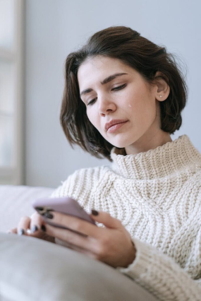 Woman in a knitted sweater looking at her smartphone indoors.