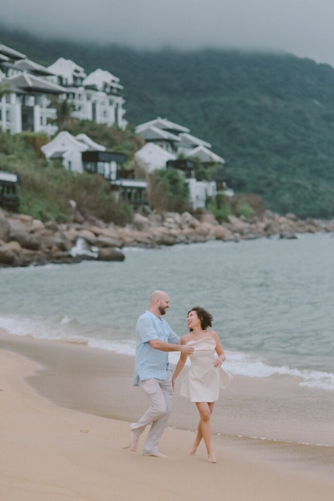 Couple walking on a sandy beach near ocean.