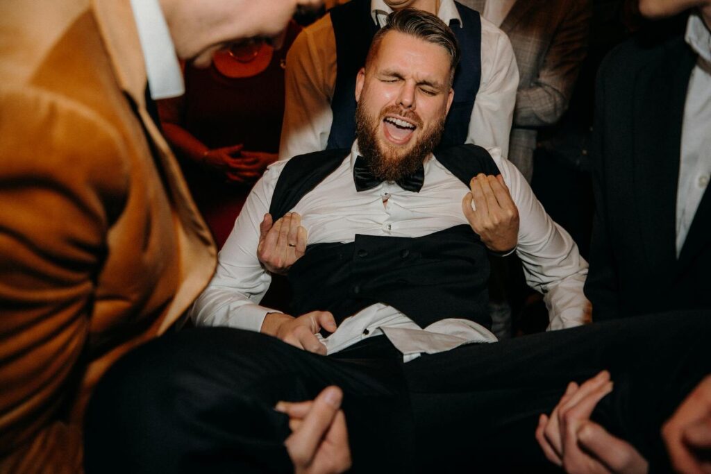 A joyful groom is lifted by friends, capturing a fun moment at a wedding reception.