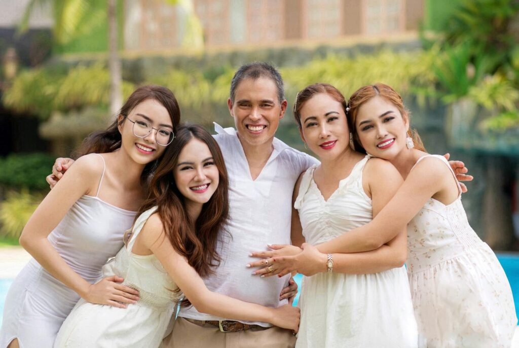 A joyful family of five embracing and smiling outdoors in bright summer attire.