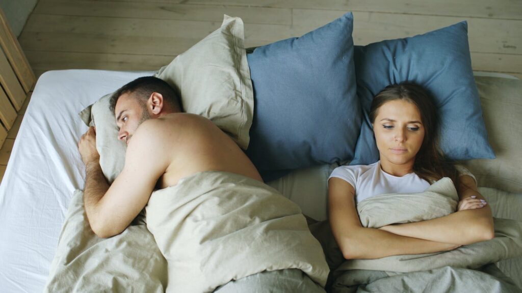 Tense couple lying apart in bed, reflecting relationship strain.
