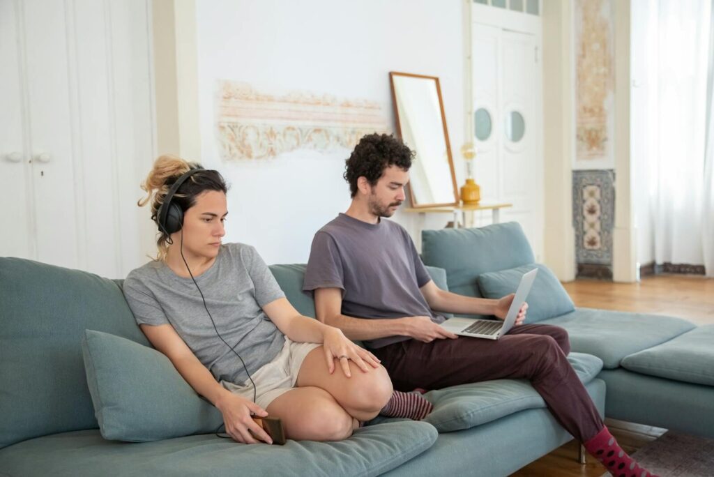 A couple relaxing on a sofa with headphones and laptop, creating a cozy home atmosphere.
